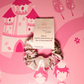 Flora Dream Scrunchie aus Satin in Rosa, Lila und Grün vor rosa Hintergrund mit Schlossmotiv.