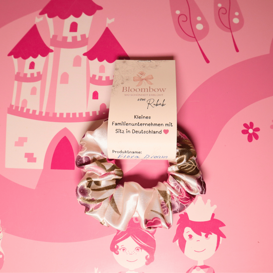 Flora Dream Scrunchie aus Satin in Rosa, Lila und Grün vor rosa Hintergrund mit Schlossmotiv.
