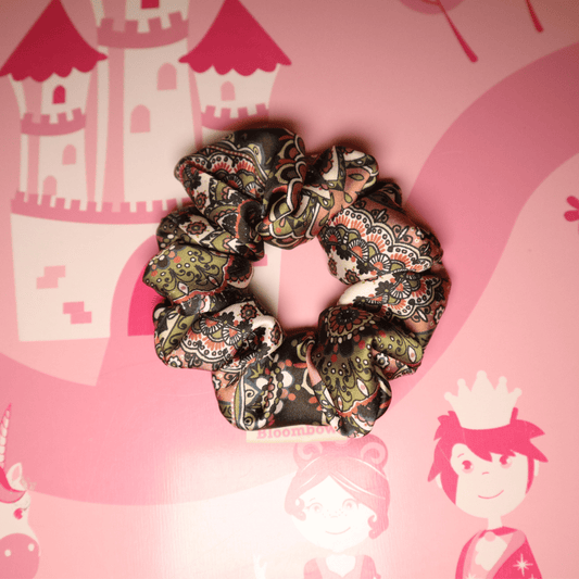 Scrunchie in Paisley-Muster mit Erdtönen, Schwarz und Grün auf rosa Hintergrund.