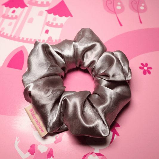 Silber satin scrunchie Moonveil auf pinkem Hintergrund.