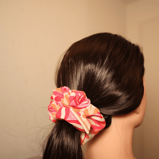 Scrunchie Melody in rosa, orange, rot mit abstraktem Herzenmuster im Haar gebunden.