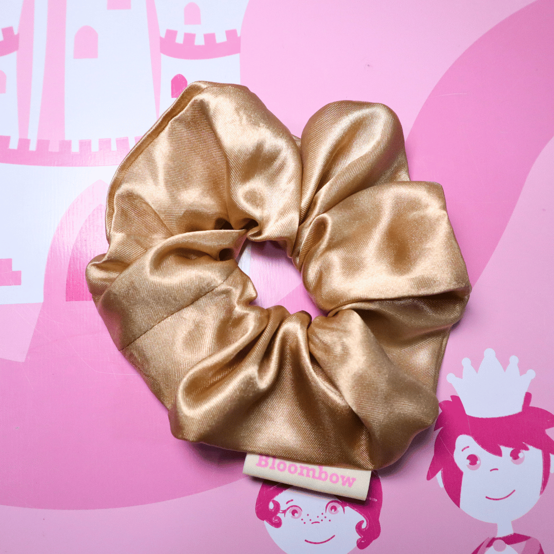 Golden satin scrunchie on pink background with Bloombow label, eco-friendly packaging.