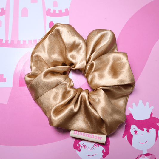 Golden satin scrunchie on pink background with Bloombow label, eco-friendly packaging.