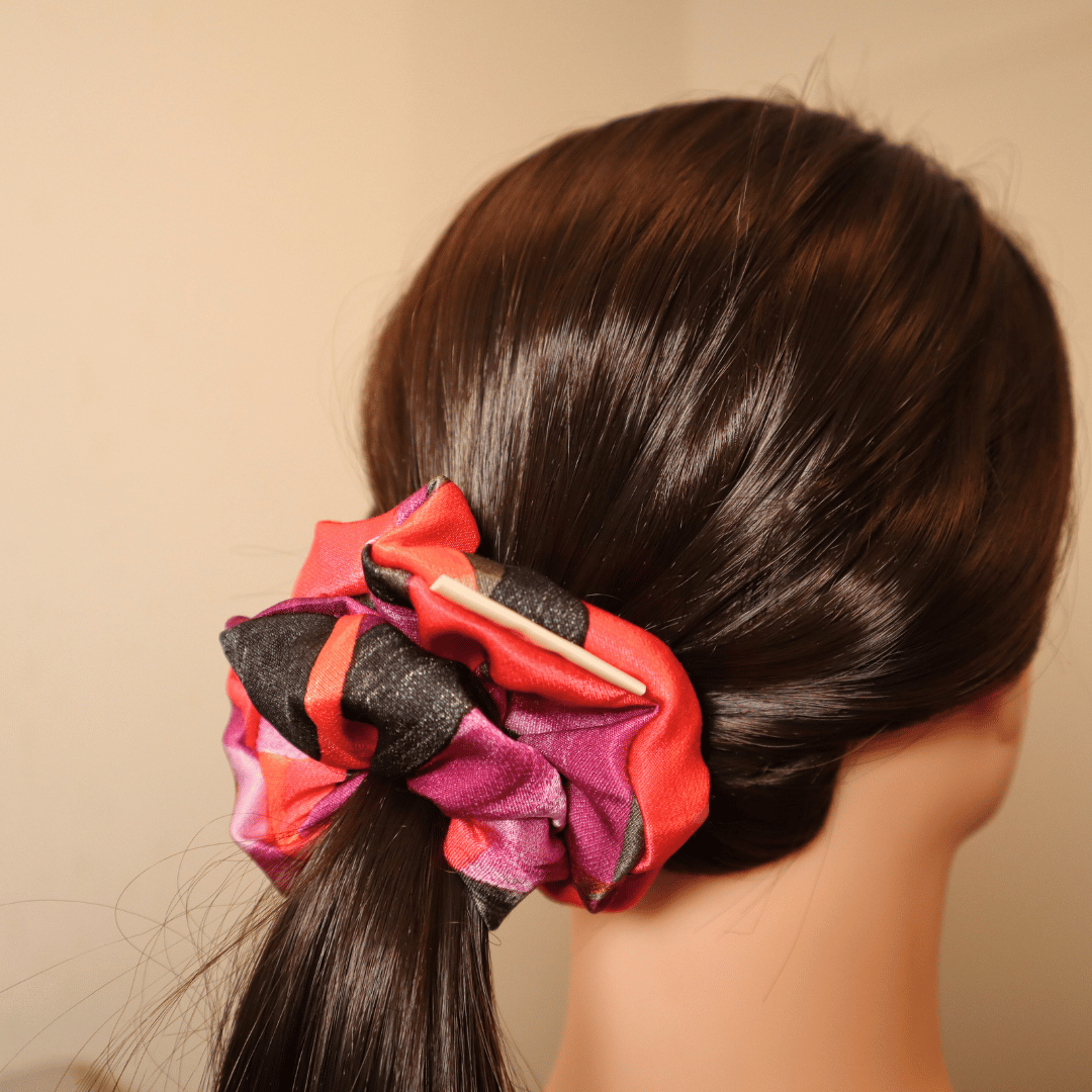 Leuchtendes Scrunchie Flare im Haar, handgefertigt, mit abstraktem rot-lila Muster.