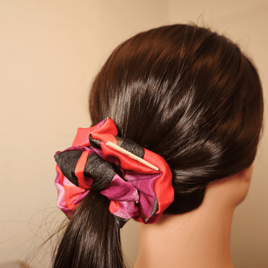 Leuchtendes Scrunchie Flare im Haar, handgefertigt, mit abstraktem rot-lila Muster.