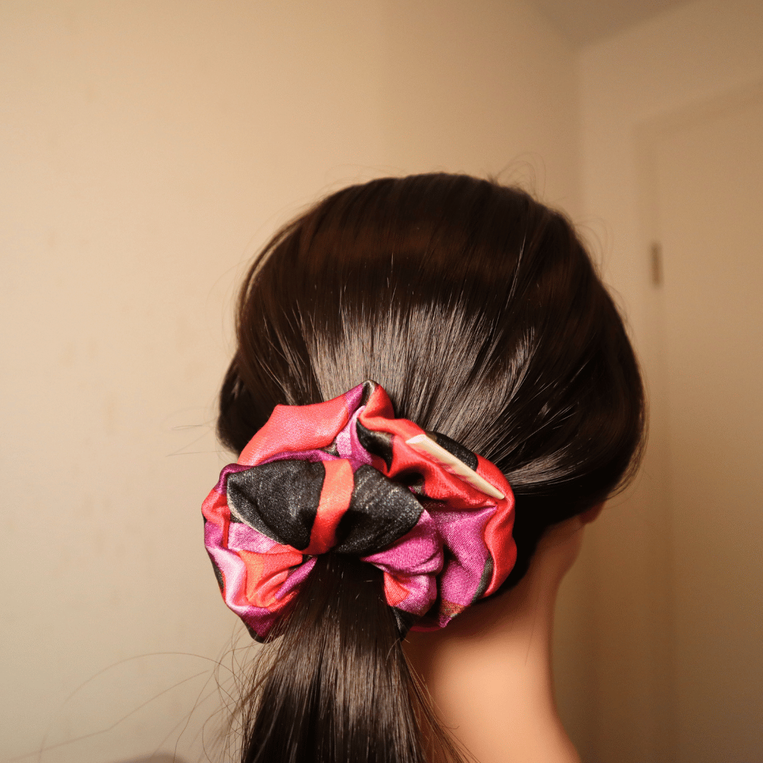 Scrunchie Flare in leuchtendem Rot, Rosa und Lila auf dunklem Haar im Pferdeschwanz.