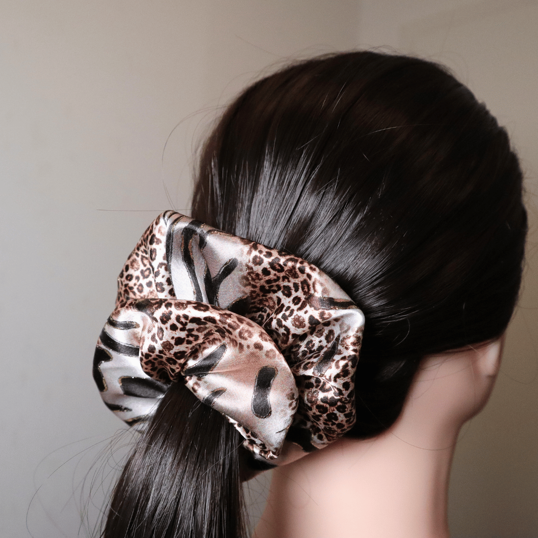 Scrunchie Tiggy in leopard print satin, providing gentle hair hold without breakage.