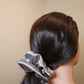 Silver satin scrunchie "Moonveil" in dark hair, stylish and gentle on hair, German handmade, eco-friendly packaging.